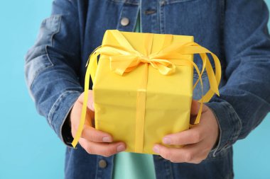 Mavi arka planda hediye kutusu olan yakışıklı genç adam, yakın plan.