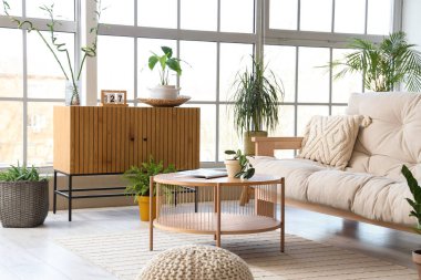 Rahat kanepesi, masası, ahşap göğüs çekmecesi ve çiçekleri olan modern oturma odasının içinde.