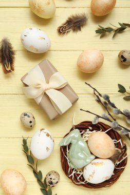 Boyanmış Paskalya yumurtaları, dalları ve sarı ahşap arka planda hediye kutusu olan bir yuva.