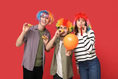 Kırmızı arka planda parti düdüğü ve balonla komik kılık değiştirmiş genç arkadaşlar. 1 Nisan kutlamaları