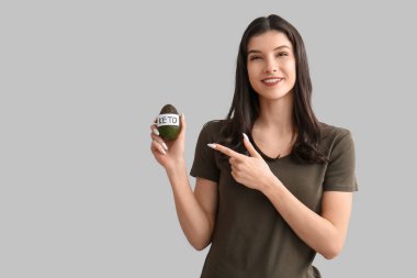 Mutlu gülümseyen genç kadın beyaz arka planda KETO sözcüğüyle avokadoyu işaret ediyor. Diyet kavramı