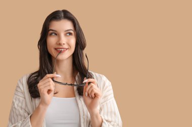 Mutlu gülümseyen genç kadın bej arka planda gözlük tutuyor.