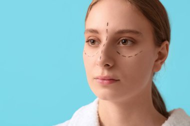 Yüzünde mavi arka planda izler olan genç bir kadın. Blepharoplasty konsepti