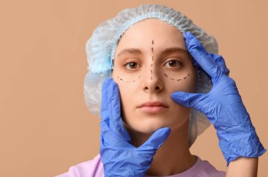 Plastik cerrah kahverengi arka planda kadının yüzünü inceliyor. Blepharoplasty konsepti