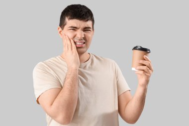 Elinde kahve fincanı olan genç adam arka planda diş ağrısından muzdarip.