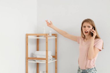 Küflü duvarlı hoşnutsuz genç kadın banyoda cep telefonuyla konuşuyor.