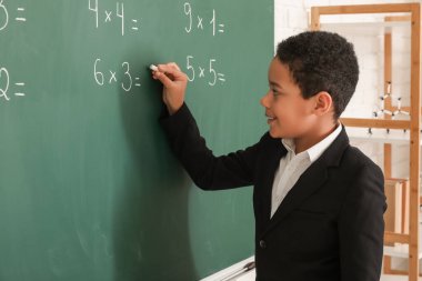 Sınıfta karatahtaya yazı yazan sevimli Afro-Amerikalı çocuk.