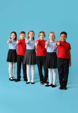Okul üniformalı bir grup şirin çocuk mavi arka planda baş parmak kaldırıyor.