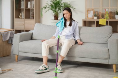 Oturma odasını temizledikten sonra kanepede oturan yorgun genç kadın.