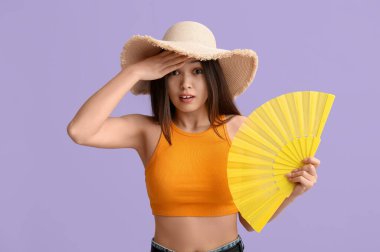 Şapkalı genç bir kadın ve yelpaze leylak arka planında sıcaktan muzdarip.