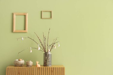 İçinde ağaç dalları ve paskalya yumurtaları olan vazo, odanın yeşil duvarının yanında klozette.