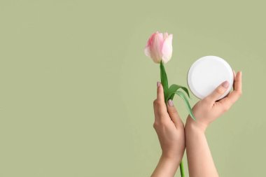 Yeşil arka planda el kremi ve lale kavanozu olan bir kadın.