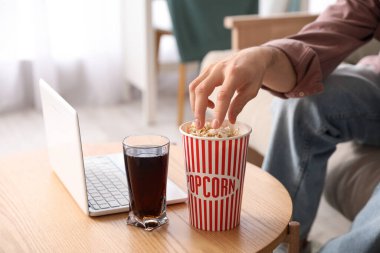 Erkek el, masadan dizüstü bilgisayarlı patlamış mısır ve odada bir bardak kola alıyor.