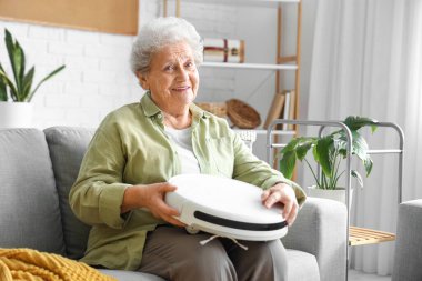 Evde kanepede oturan robot elektrikli süpürgeyle mutlu bir son sınıf kadını.