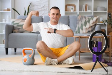 Evde telefonda spor videosu kaydederken kaslarını gösteren kettlebell 'li bir erkek antrenör.