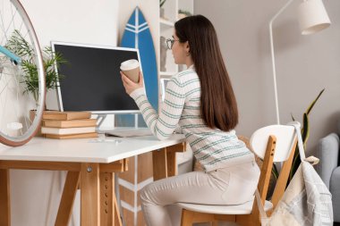 Evde bilgisayar kullanan kahve fincanı olan bir kız öğrenci.