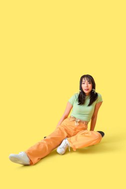 Sarı arka planda kaykaylı fiyonklu şık genç Asyalı kadın.