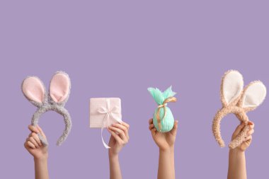 Hediye yumurtalı kadın elleri, tavşan kulaklıkları ve menekşe arkaplanda hediyeler. Paskalya konsepti.