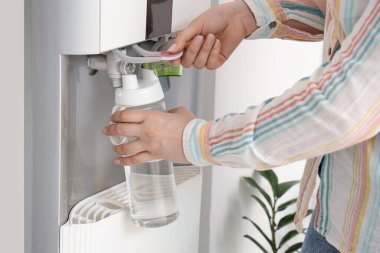 Beyaz duvarın yanındaki soğutucunun filtreli suyla dolduran kadın.