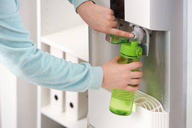 Yeşil şişeyi soğutucudan filtrelenmiş suyla dolduran kadın elleri