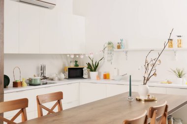 Mutfaktaki yemek masasında ağaç dalları ve Paskalya yumurtaları olan vazo.