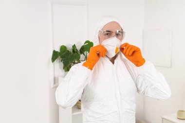 Oda dezenfeksiyonundan önce tehlikeli madde kıyafeti giyen bir erkek işçi.