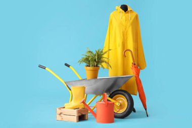 Yağmurluk, şemsiye, bahçe aletleri ve mavi arka planda el arabası
