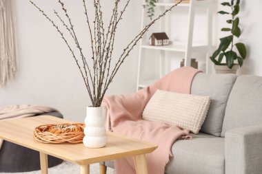 Oturma odasındaki masada söğüt dalları ve pasta olan vazo.