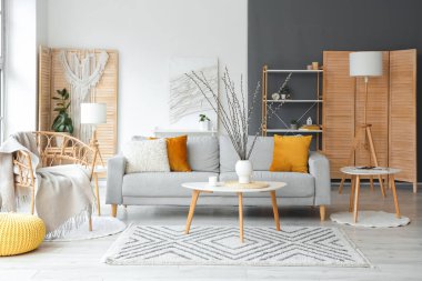 Oturma odasının içinde kanepe, koltuk ve vazoda söğüt dalları var.