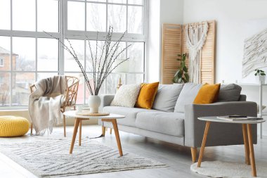 Oturma odasının içinde kanepe, koltuk ve vazoda söğüt dalları var.