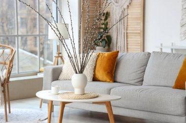 Oturma odasındaki masada söğüt dalları ve fincanı olan bir vazo.