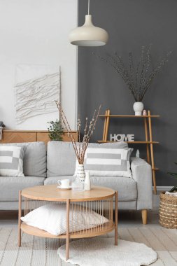 Kanepesi ve vazolarında söğüt dalları olan modern oturma odasının içinde.