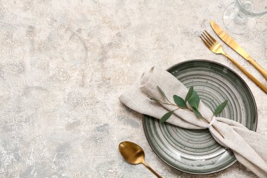 Altın çatal bıçak takımları ve gri arka planda yaprakları olan güzel bir masa.