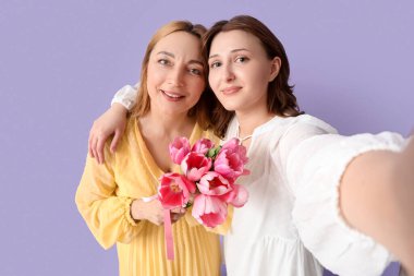 Bir buket lale ile güzel olgun bir kadın ve kızı leylak arka planda selfie çekiyor. Anneler Günü kutlaması