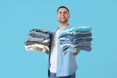 Mavi arka planda bir yığın elbisesi olan genç adam.