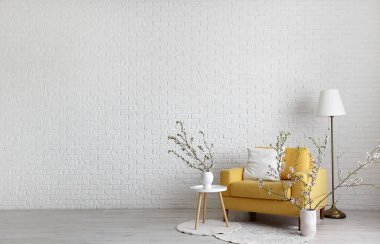 Çiçek açan dalları olan vazolar ve aydınlık oturma odasının içinde sarı koltuklar.