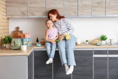 Küçük kız ve annesi mutfakta bir buket nergisle. Anneler Günü