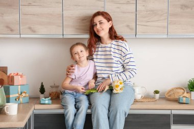 Küçük kız ve annesi mutfakta bir buket nergisle. Anneler Günü