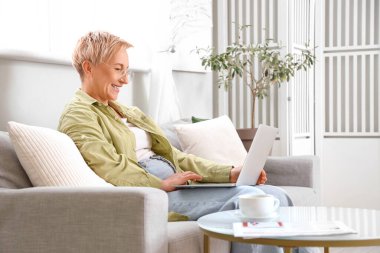 Evde kanepede dizüstü bilgisayarla çalışan olgun bir kadın programcı.