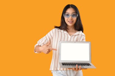 Genç bayan Asyalı programcı sarı arka planda dizüstü bilgisayarı işaret ediyor