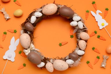 Turuncu arka planda yumurta ve tüylerden yapılmış Paskalya çelengi.