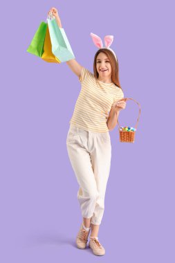 Tavşan kulaklı genç bir kadın alışveriş torbaları ve leylak arkaplanda Paskalya yumurtaları.