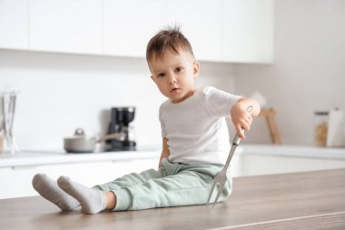 Keskin çatallı küçük çocuk mutfaktaki masada oturuyor. Tehlikedeki çocuk