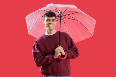 Kırmızı arka planda şeffaf şemsiyeli genç adam