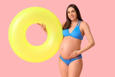 Pembe arka planda şişme yüzüğü olan hamile bir kadın. Seyahat kavramı