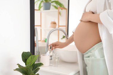 Genç hamile kadın banyoda diş fırçası alıyor.