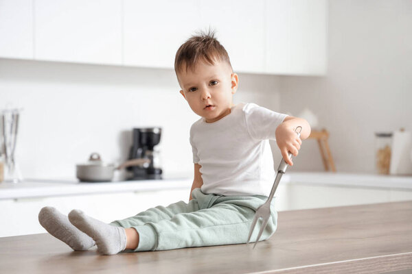 Мальчик с острой вилкой сидит на столе на кухне. Ребенок в опасности