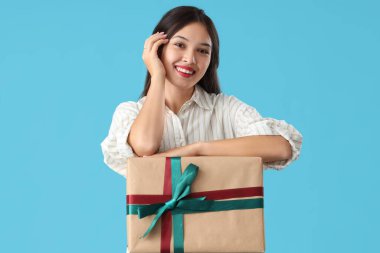 Mavi arka planda hediye kutusu olan güzel bir Asyalı kadın.