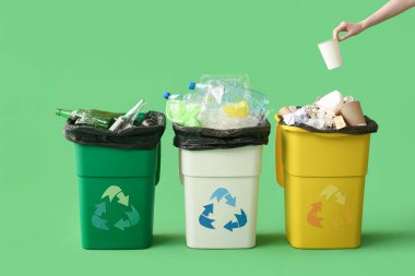 Yeşil arka planda çöp ve geri dönüşüm kutularını sıralayan gönüllü kadın