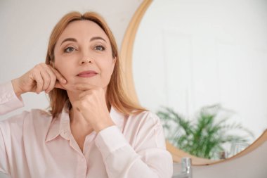 Güzel, olgun bir kadın tuvalette yüz geliştirme egzersizi yapıyor.